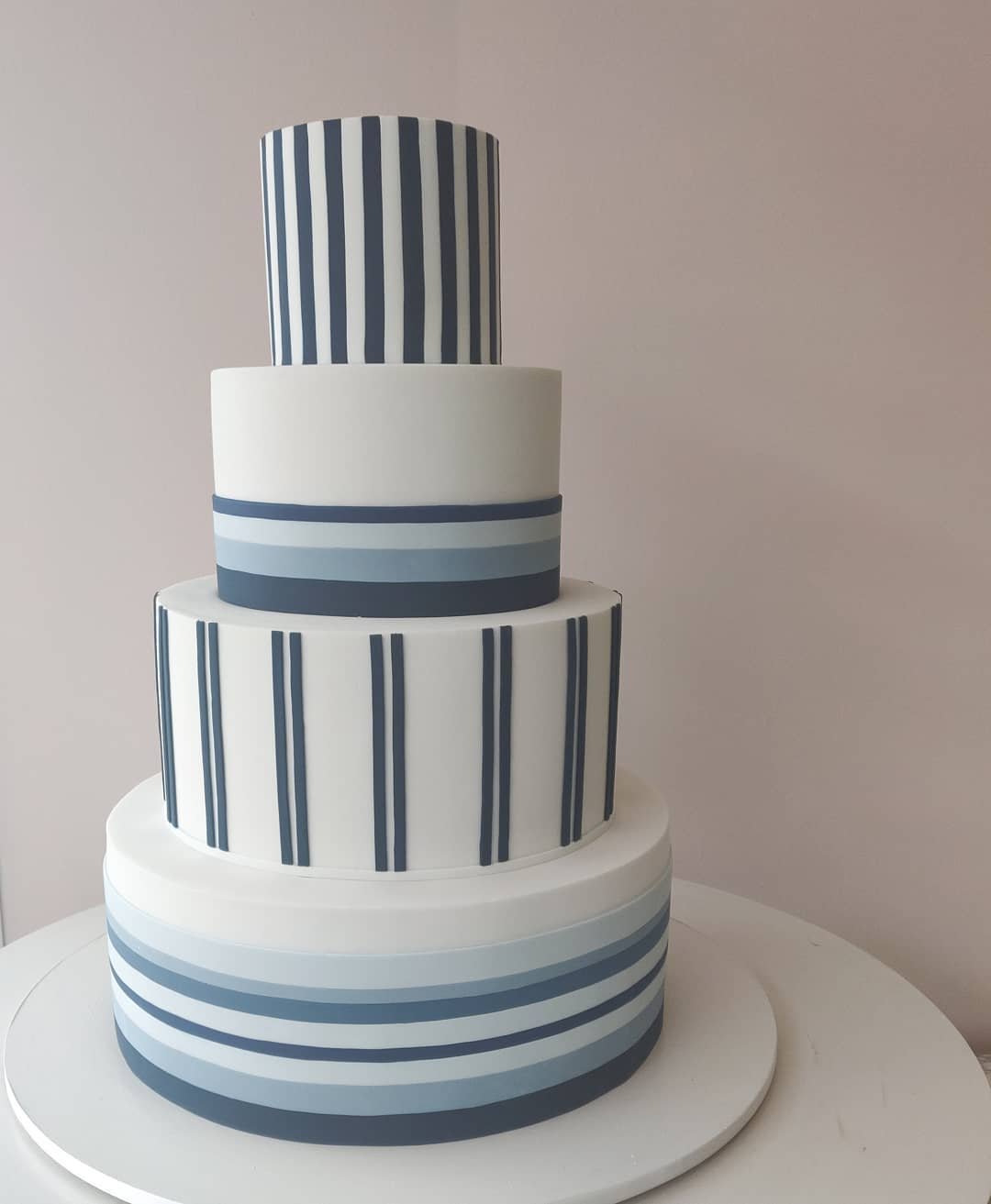 A four-tier wedding cake featuring stripes in varying shades of blue and white, designed with clean lines and a modern aesthetic.