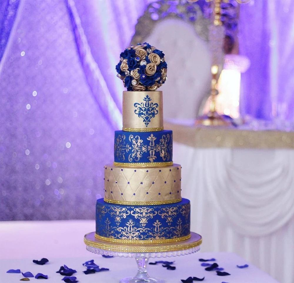 A blue and gold wedding cake with intricate designs and a rose bouquet on top.