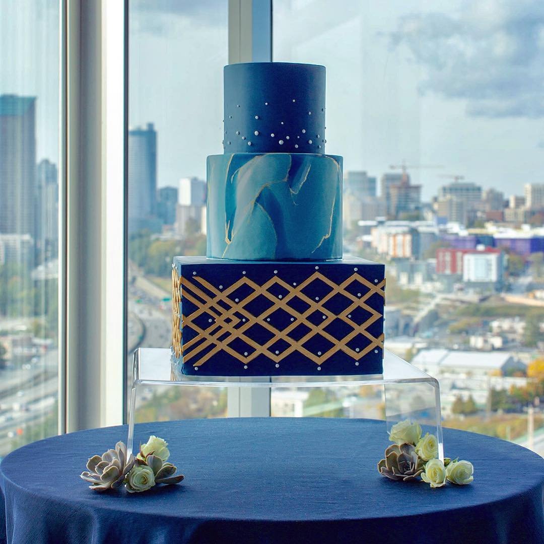 A three-tier cake with blue marbled layers and gold geometric designs.