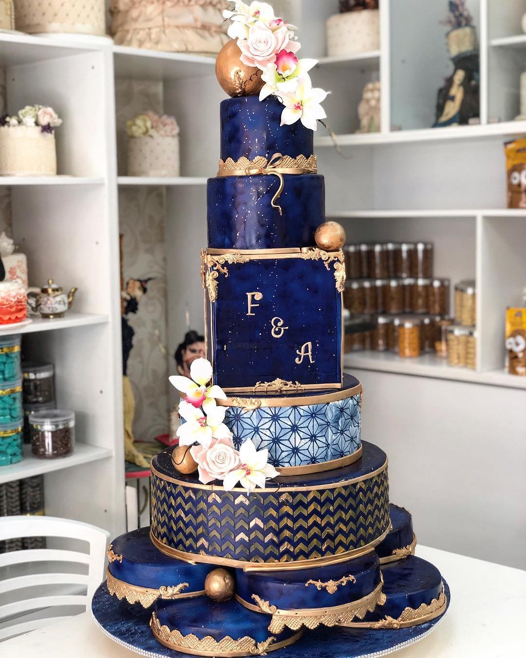 A five-tier cake with navy blue and gold designs, decorated with pink flowers and initials "F & A."