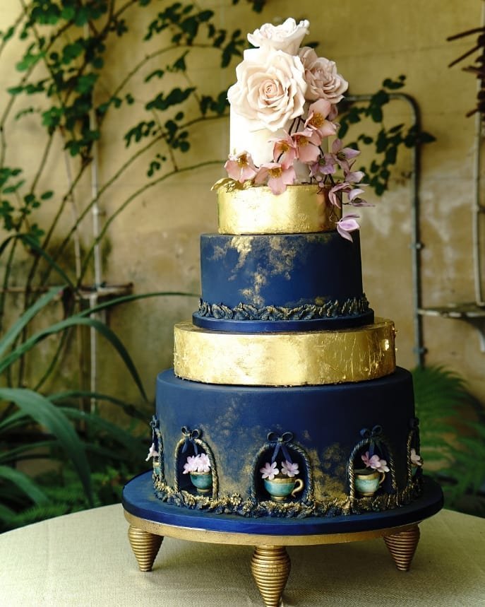 A four-tier cake with navy blue and gold, adorned with pink roses and orchids.