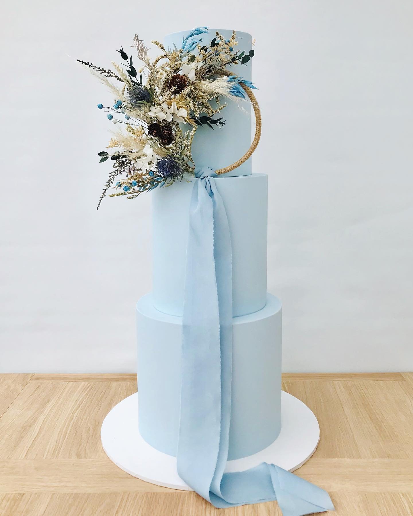 A light blue three-tier cake with floral decoration and a ribbon.