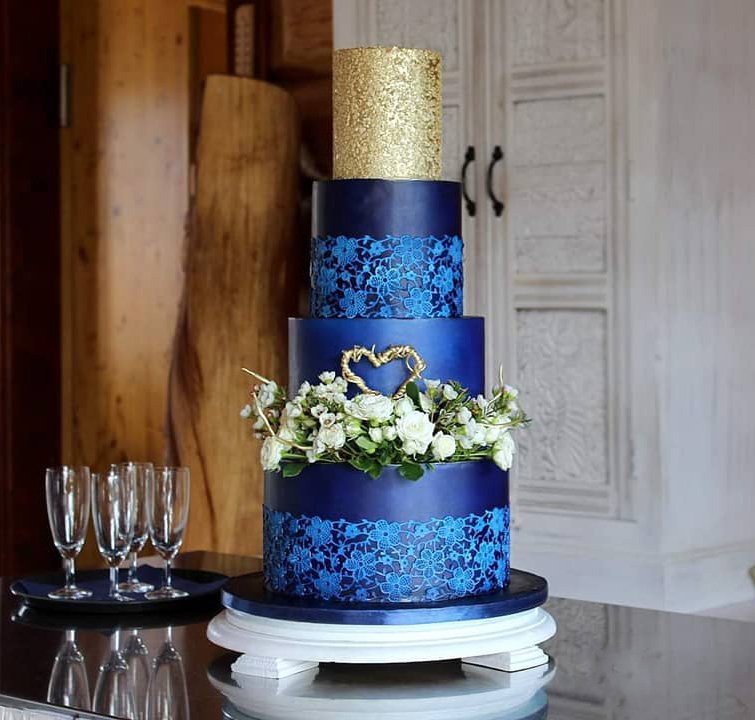 A three-tier cake with navy blue and gold, adorned with white flowers.