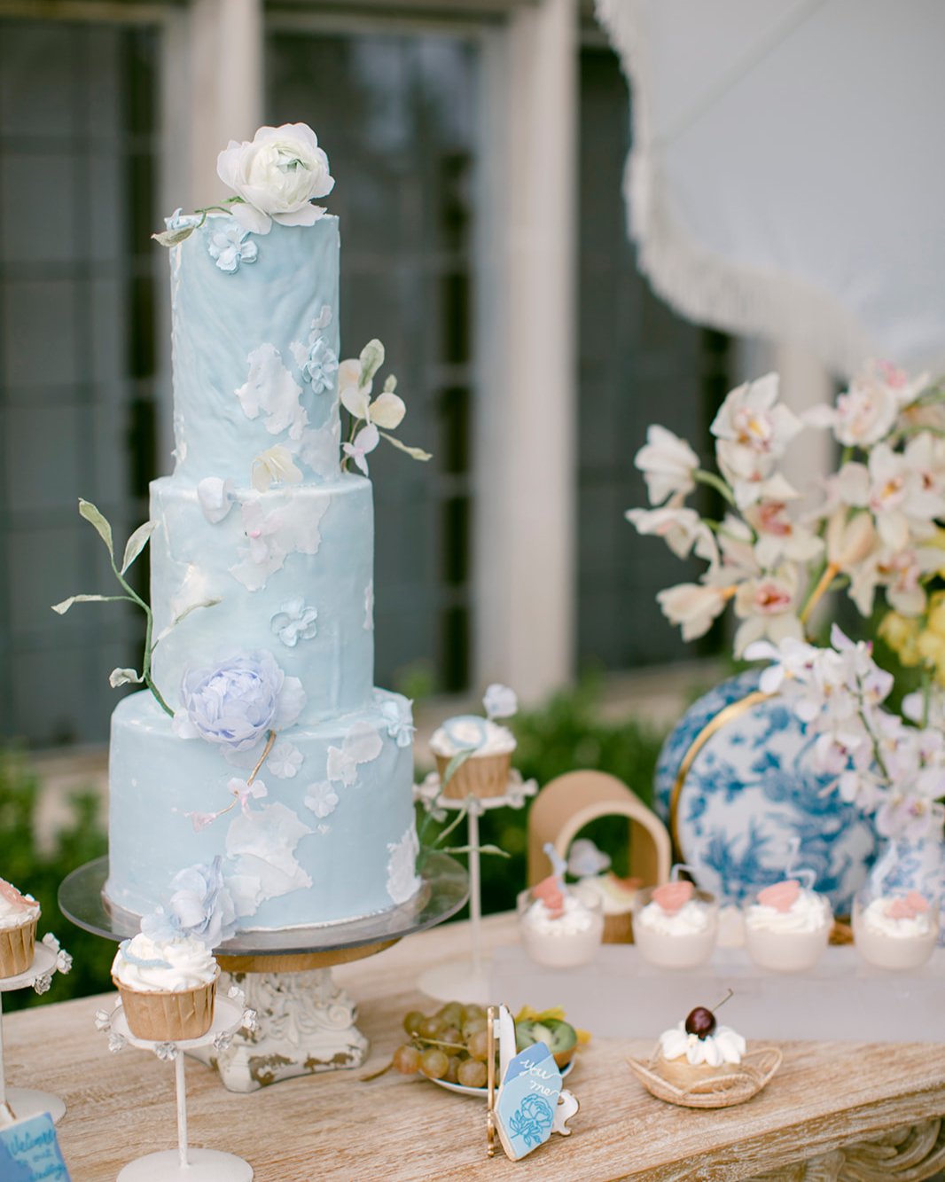 Three-tiered cake with floral decorations on a table surrounded by desserts.