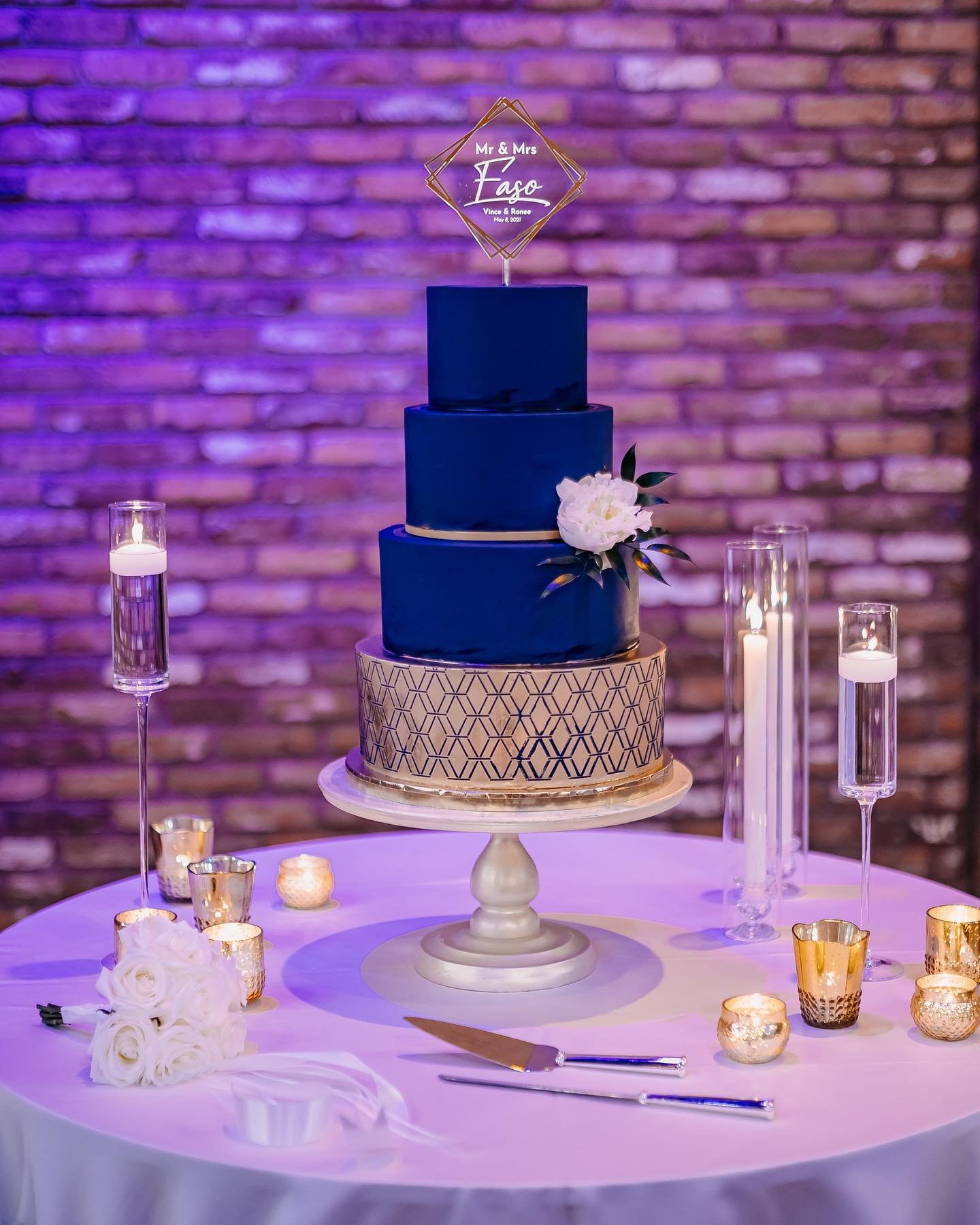 A three-tier cake with navy blue and gold, topped with a white rose.