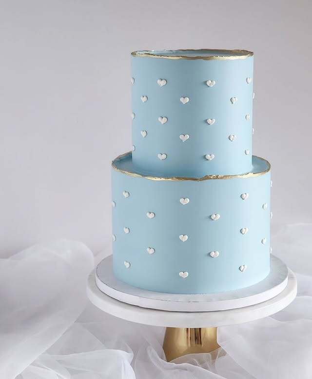 Two-tier light blue cake with white heart decorations and gold trim.