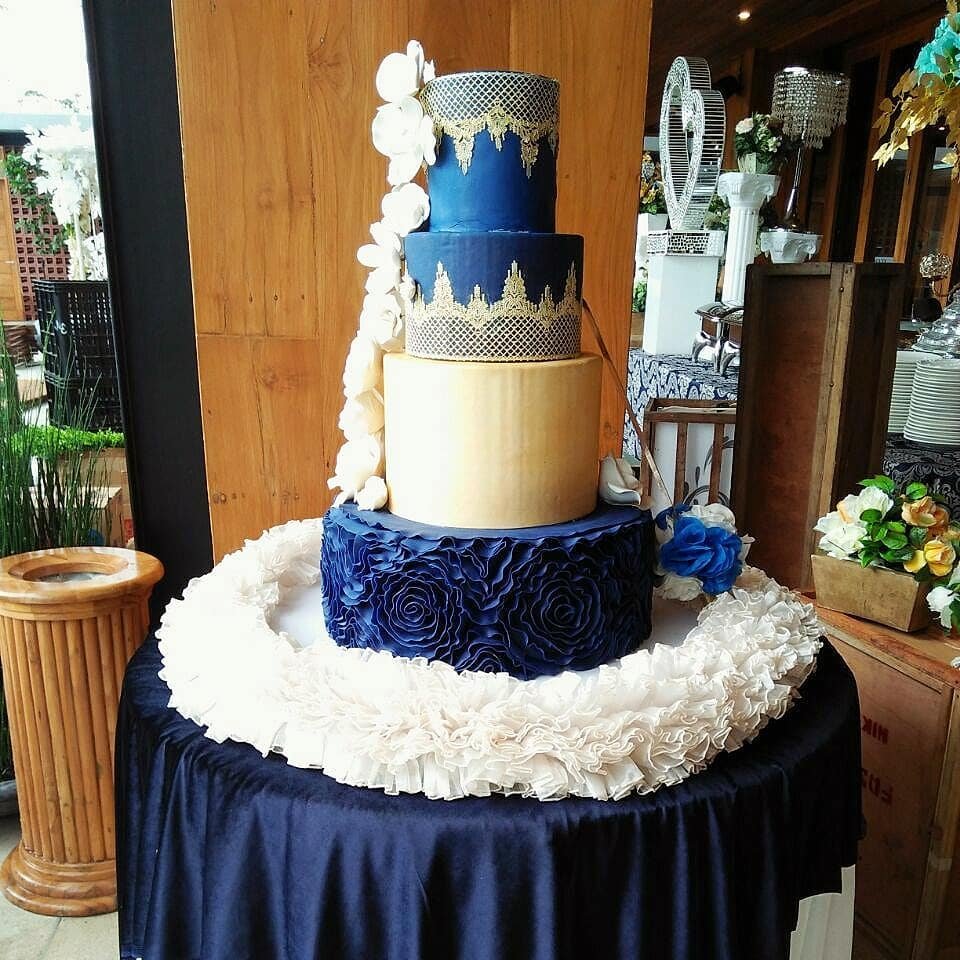 A four-tier cake with navy blue and gold, decorated with floral designs.