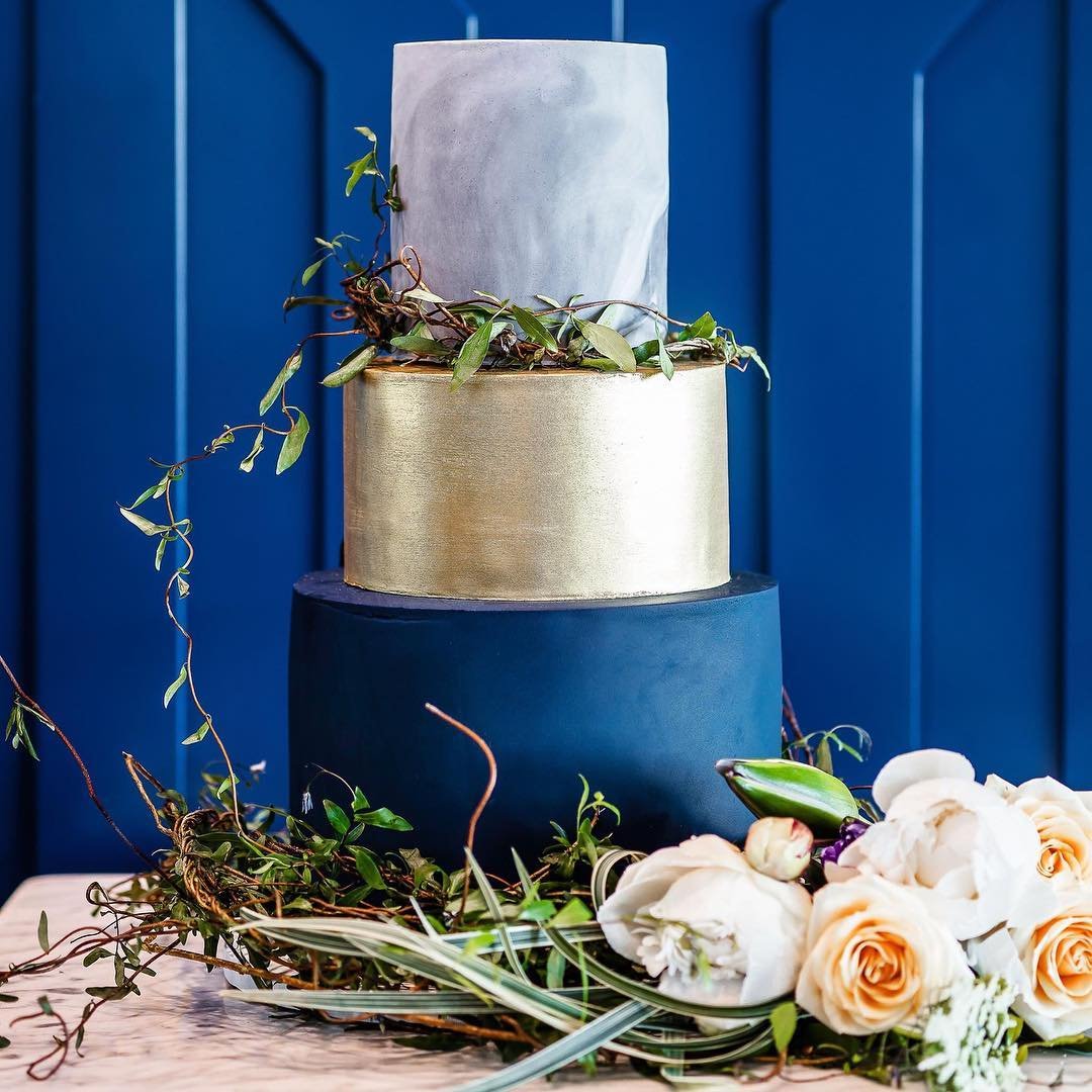 A modern three-tier cake with a gold layer and floral accents.