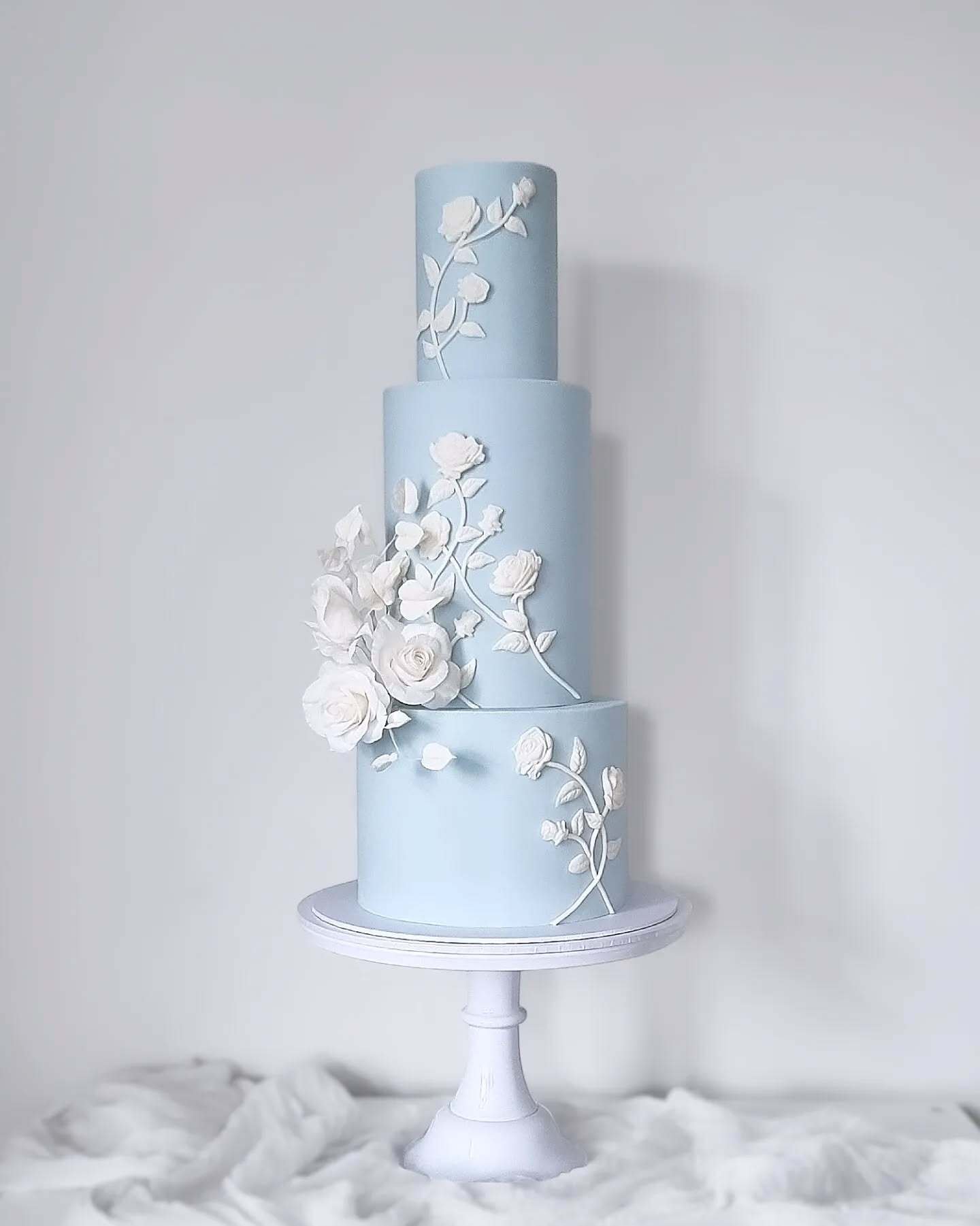 Three-tier blue cake with white floral decorations.