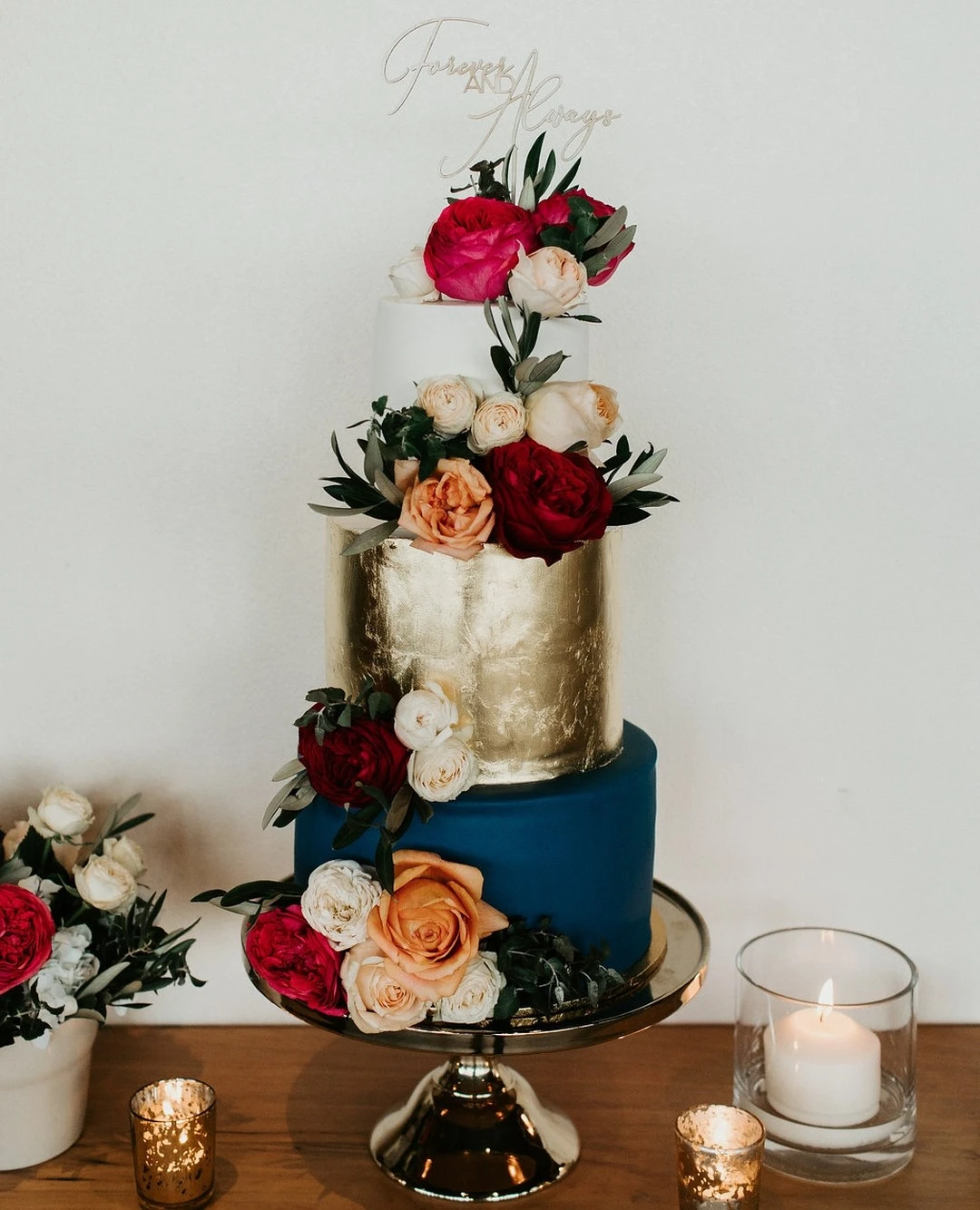 A three-tier cake with gold, white, and blue, decorated with colorful flowers.