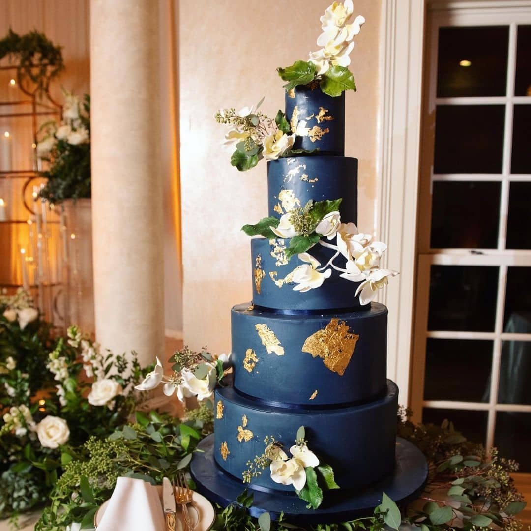 A five-tier cake with navy blue and gold leaf, decorated with white orchids.