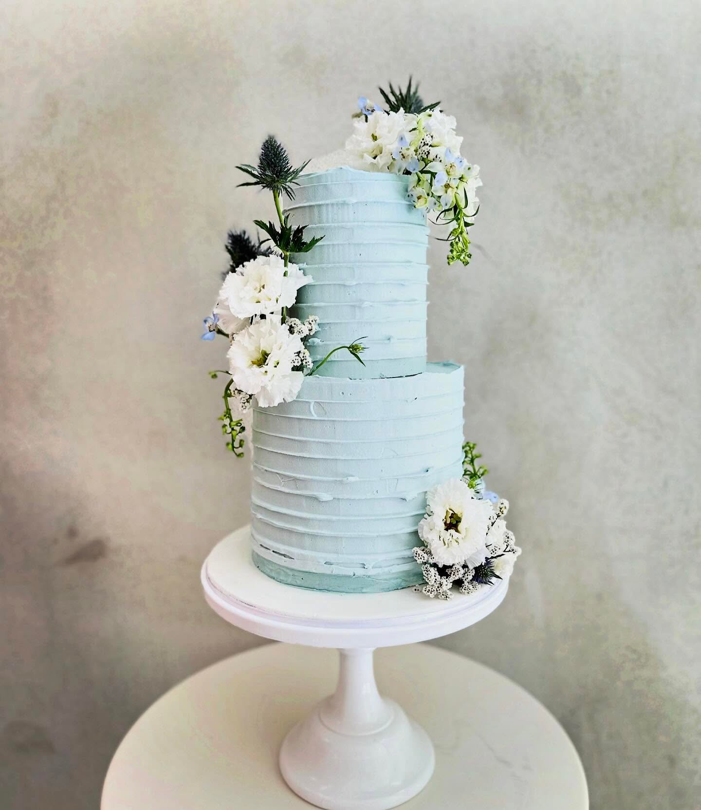 Two-tiered cake with blue frosting and floral decorations.