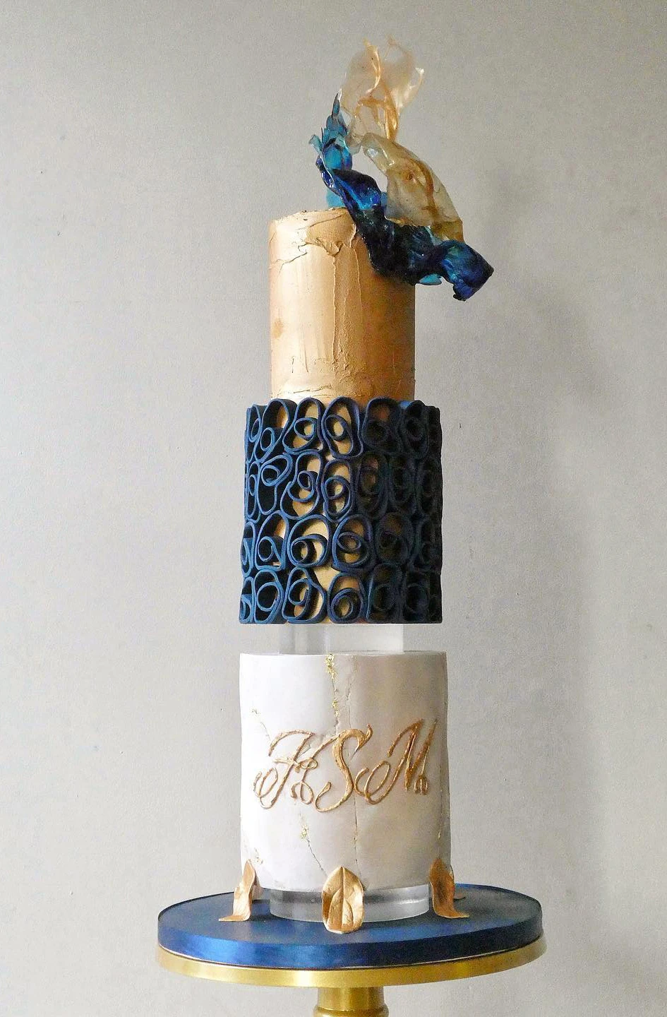 A three-tier cake with gold, navy blue, and white, featuring artistic designs.