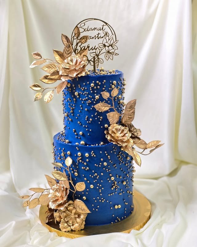 A two-tier cake with blue and gold, decorated with pearls and floral accents.