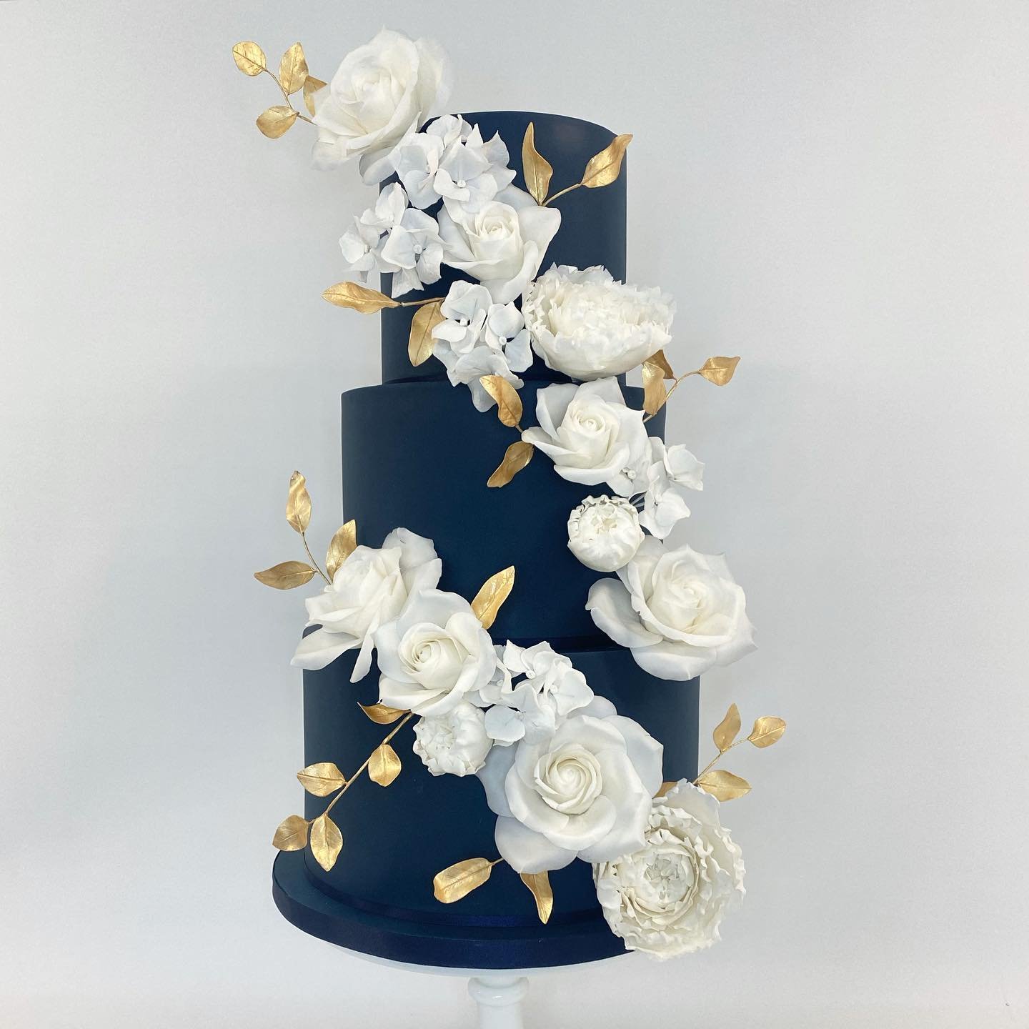 Three-tiered navy blue wedding cake adorned with white flowers and gold leaves.