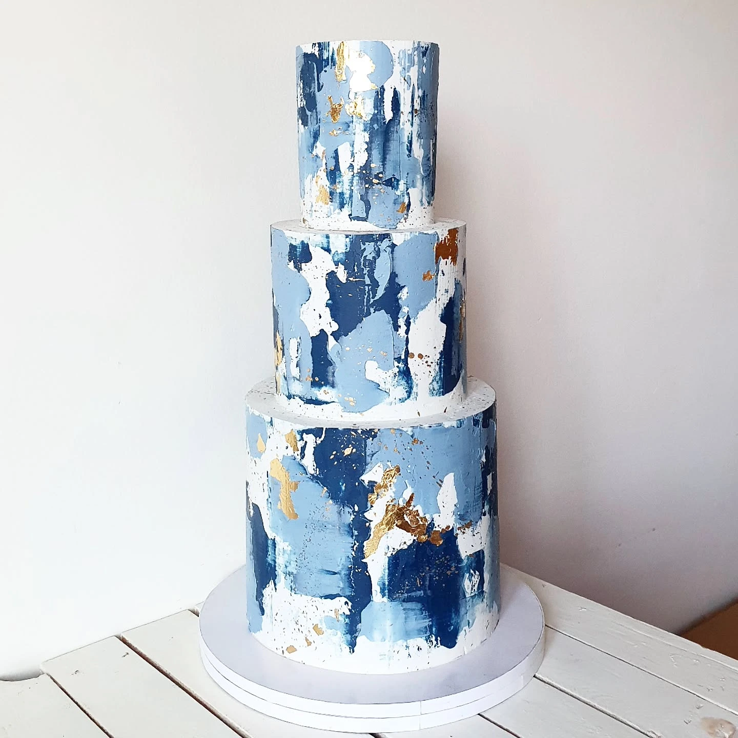 Three-tiered wedding cake featuring an abstract blue and white design with gold accents.