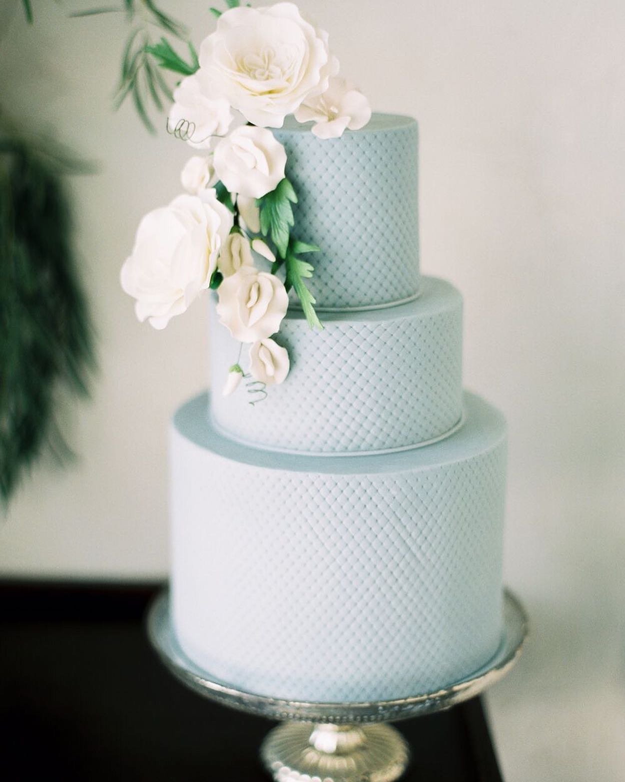 Light blue wedding cake with quilted pattern and white sugar flowers.