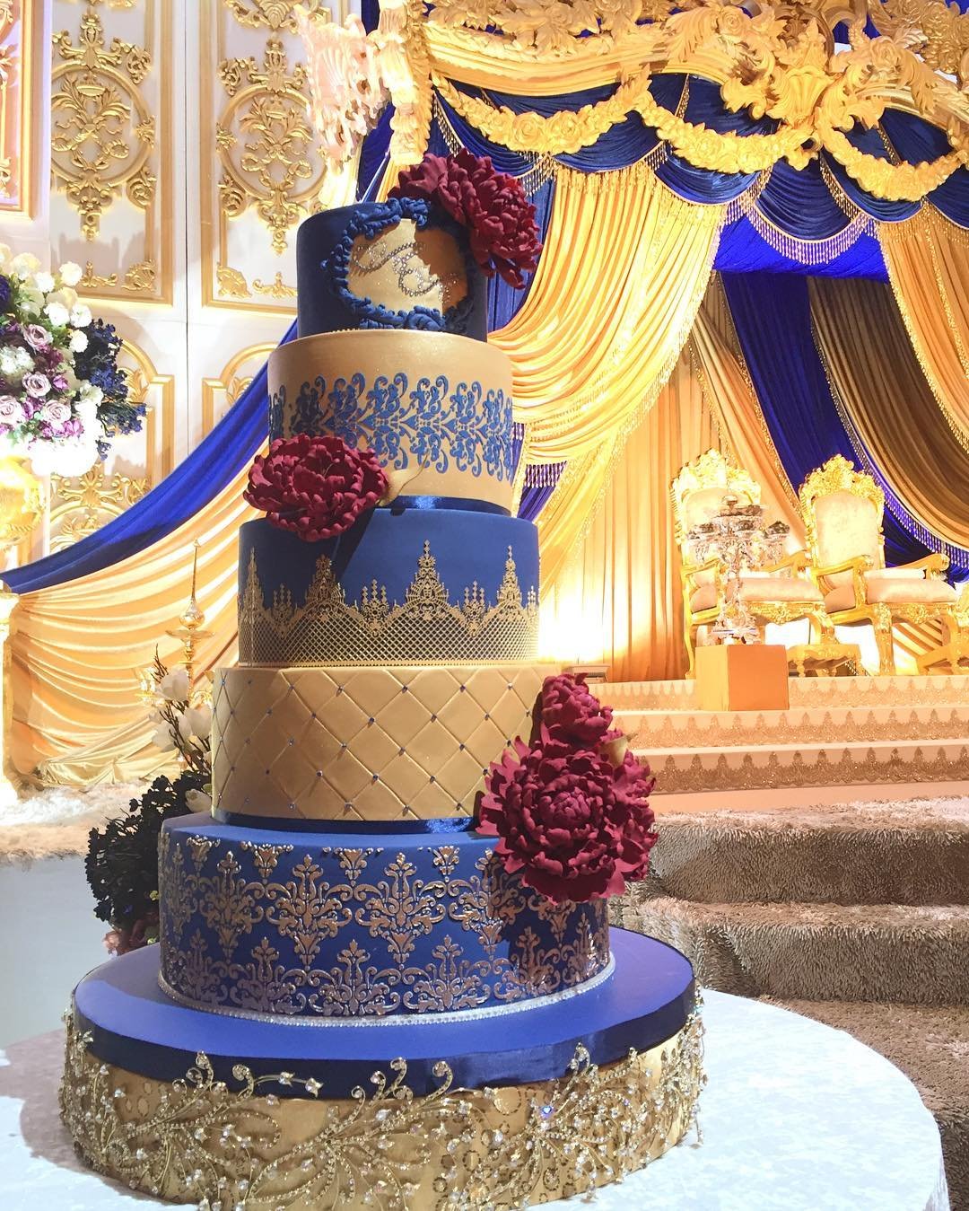 Multi-tiered royal blue and gold cake with red flowers.