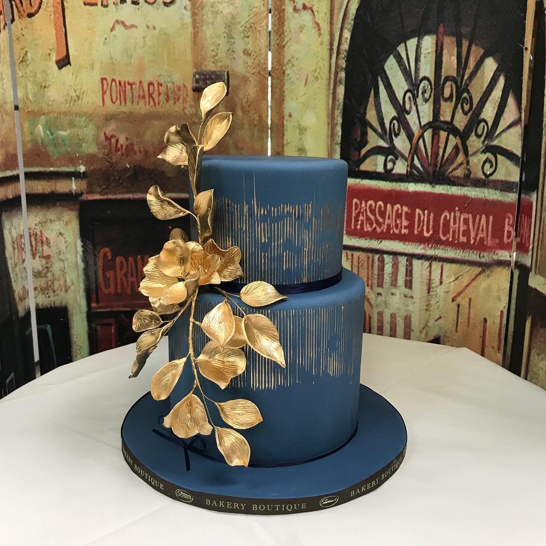 A two-tier cake in navy blue with gold accents and a floral decoration.