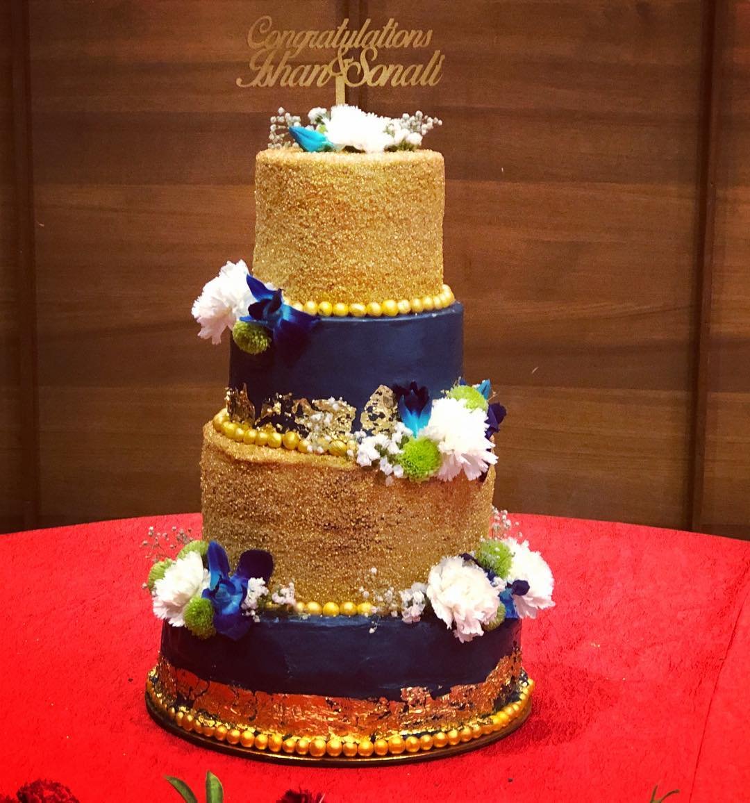 A three-tier celebration cake with blue and gold layers, floral decorations, and a "Congratulations" topper