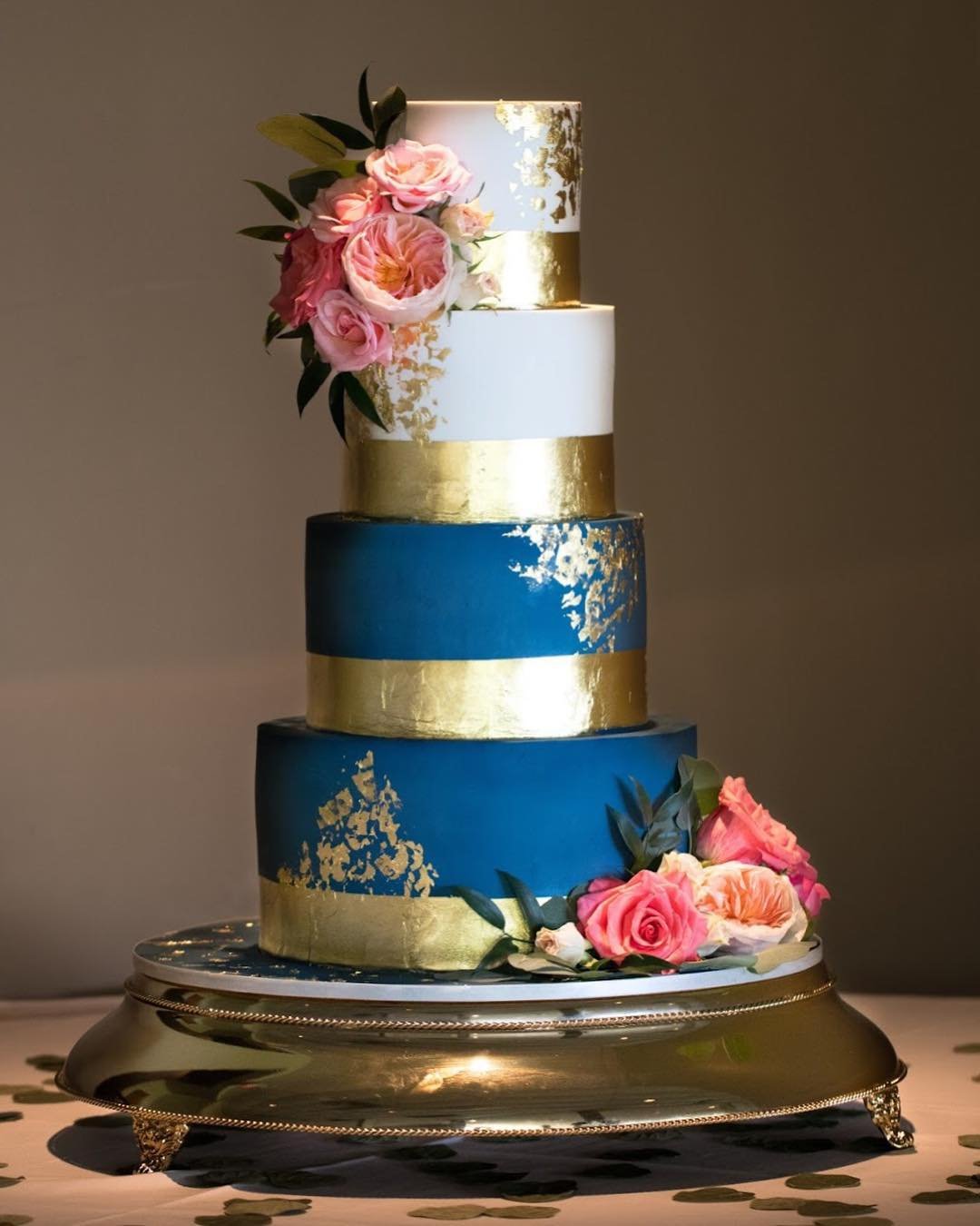 A three-tier cake with blue and white layers, gold accents, and pink floral decorations.