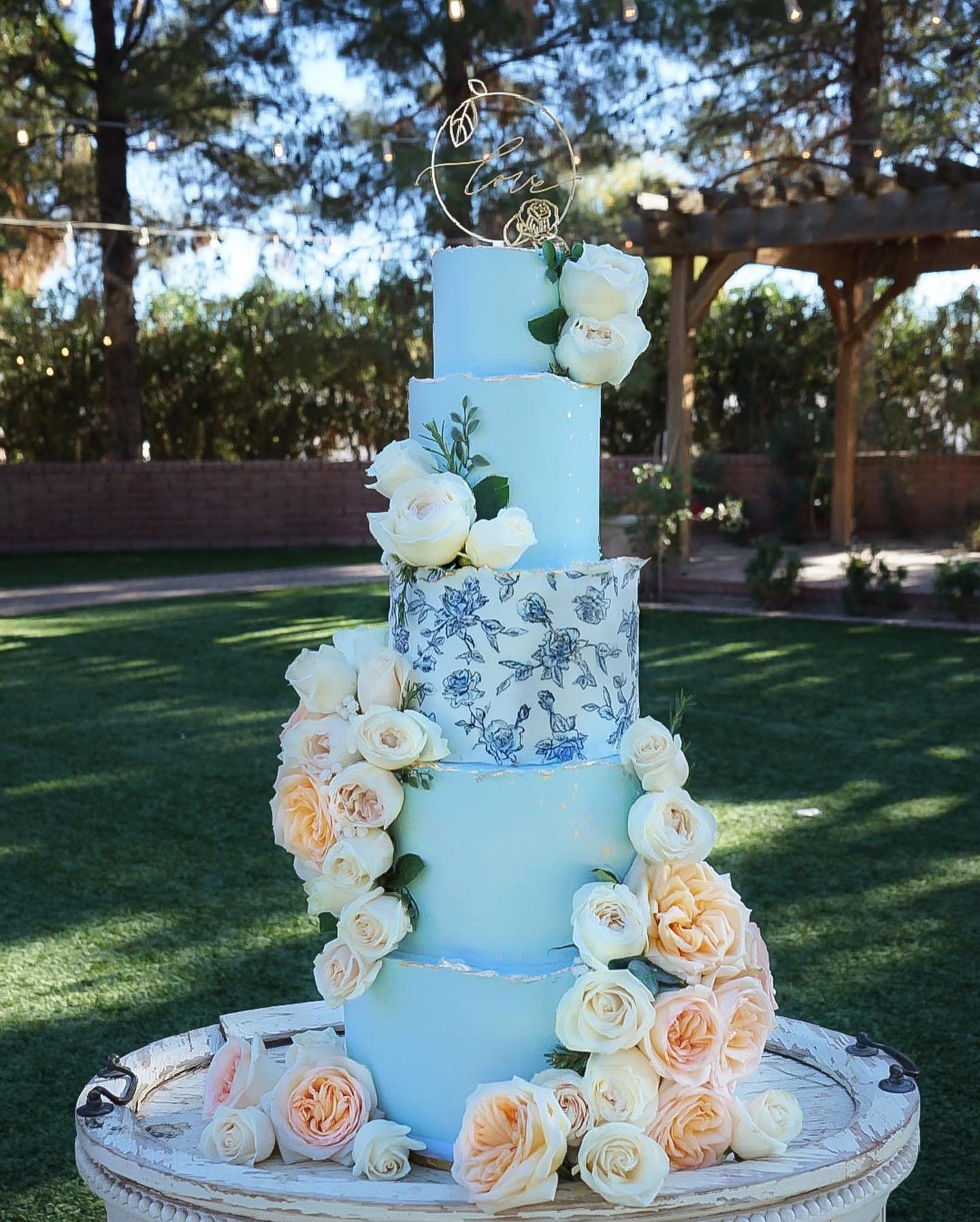 Four-tiered wedding cake with white and peach roses and a "love" topper.