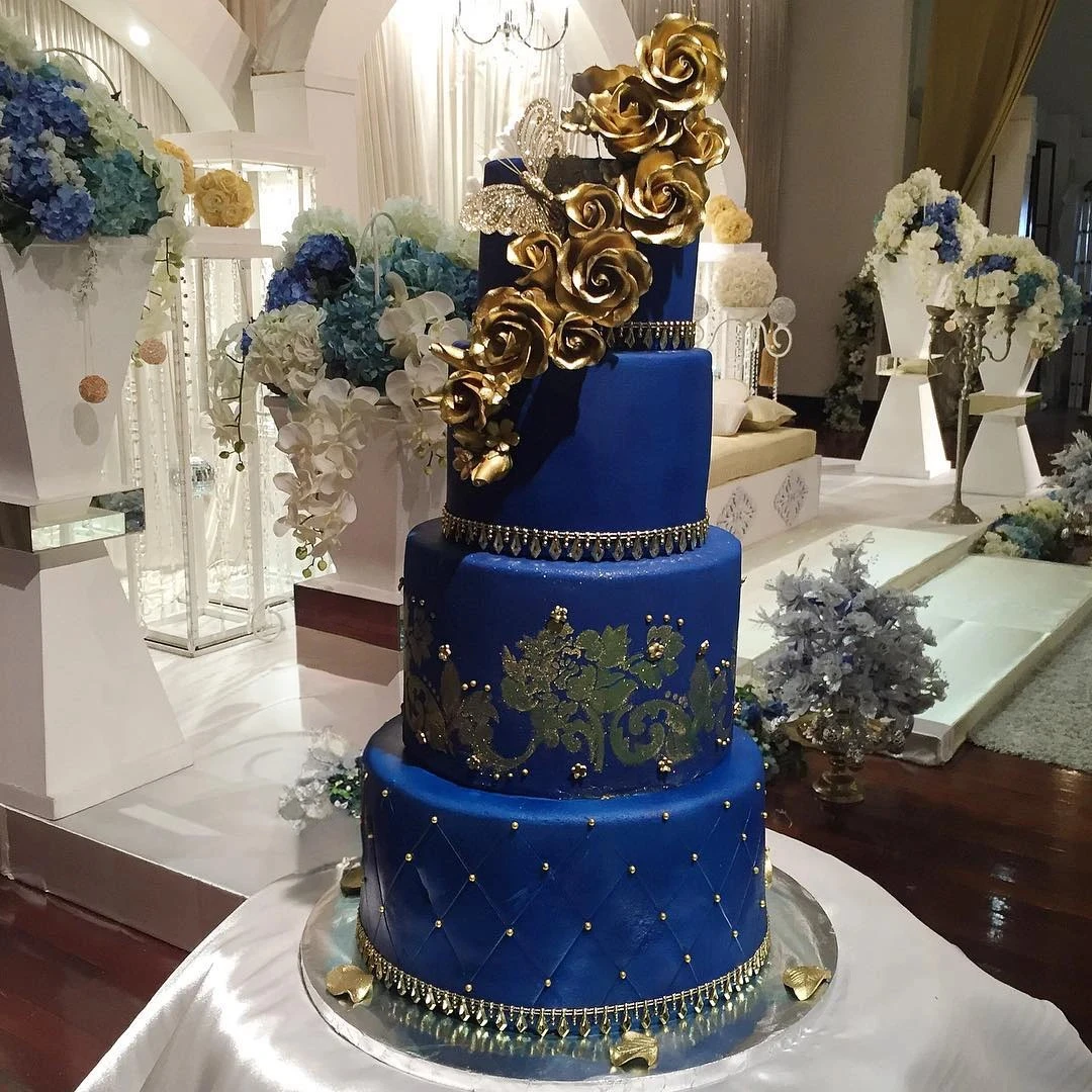 A five-tier cake with blue and gold designs, embellished with golden roses.