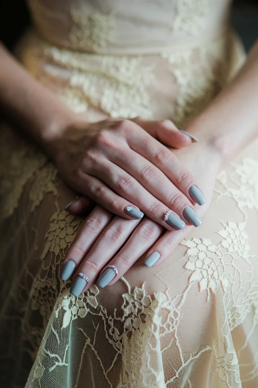 Hands with grey nails and crystal accents resting on lace fabric.