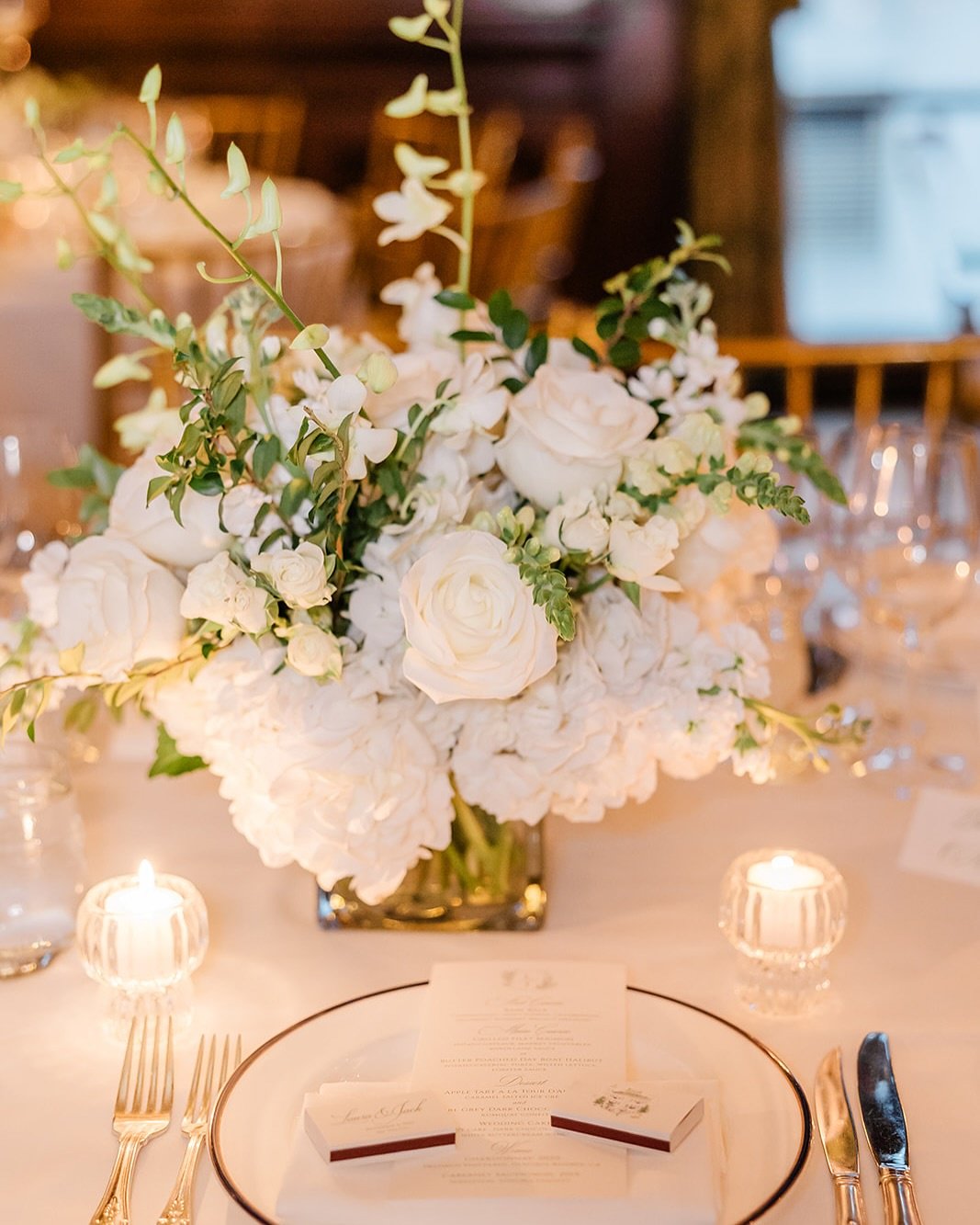 White roses, hydrangeas, and orchids in a square glass vase.