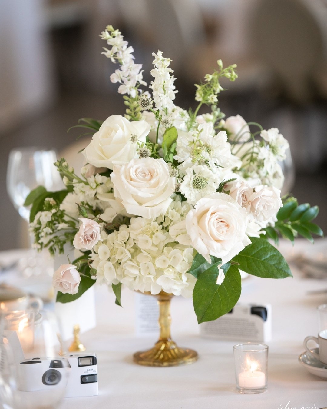 White roses, hydrangeas, and other white flowers in a gold vase.