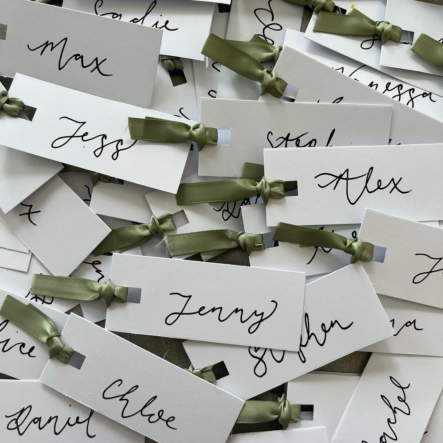 Several sage green rectangular place cards with handwritten names, each adorned with a gold wax seal and a small sprig of dried baby's breath.