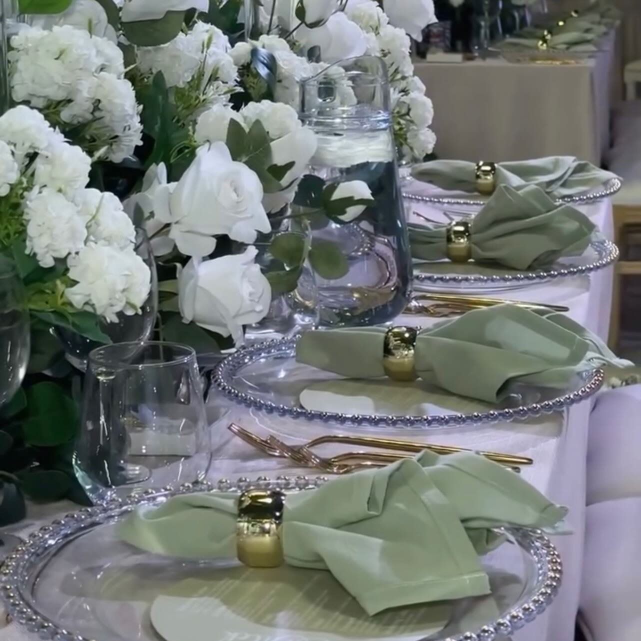 A close-up of a place setting featuring a sage green linen napkin secured with a gold napkin ring, on top of a white plate.
