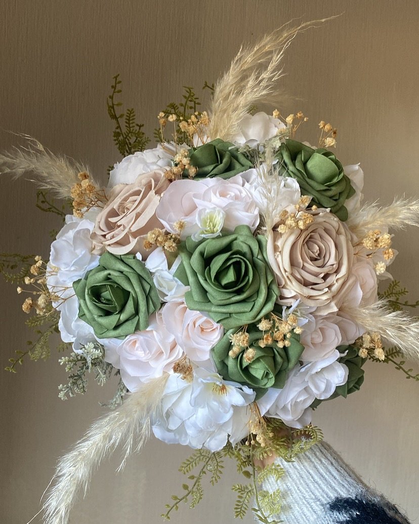 A round bridal bouquet featuring sage green, blush, and white roses, accented with pampas grass and dried filler flowers.
